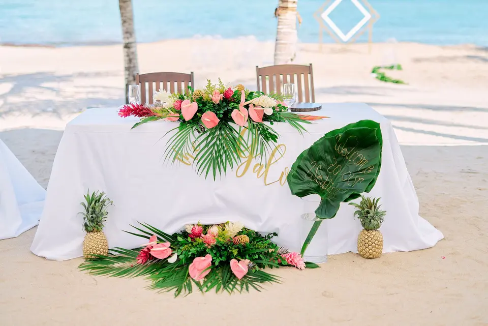 Exquisitely decorated bride and groom's table at a wedding, featuring elegant floral arrangements, with the ocean in the background.